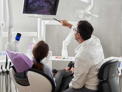 A dentist shows their patient x-rays while the patient sits back in their chair.